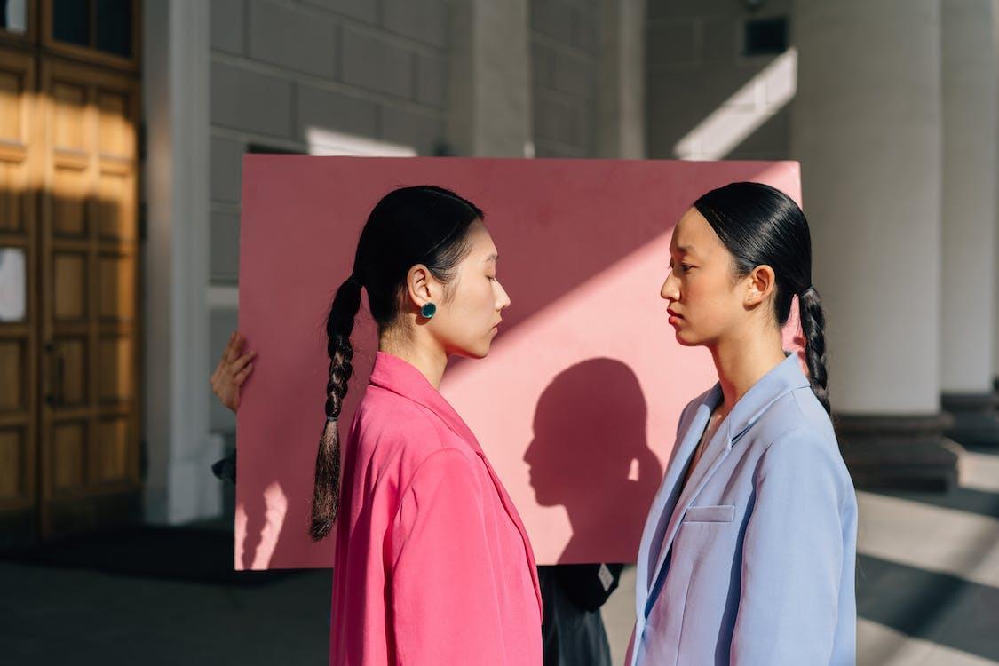 Free Woman in Pink Jacket Standing in Front of Woman in Blue Jacket Beside Pink Paper Stock Photo